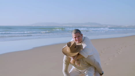 Portrait-of-happy-senior-couple-having-piggyback-ride-on-beach
