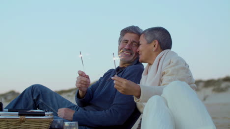 Happy-senior-Caucasian-couple-holding-sparkler-and-enjoying-time-together-on-the-beach
