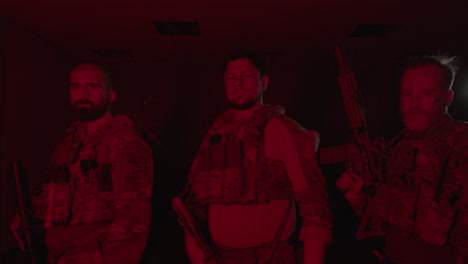 Front-view-of-soldiers-in-bulletproof-vests-standing-in-dark-room-and-looking-at-camera