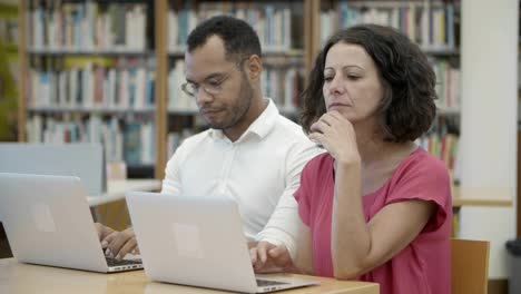 Dos-Personas-Pensativas-Que-Trabajan-Con-Una-Laptop-En-La-Biblioteca-Pública