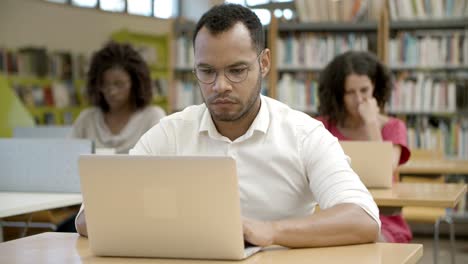 Vista-Frontal-Del-Hombre-Afroamericano-Enfocado-Usando-Una-Computadora-Portátil-En-La-Biblioteca