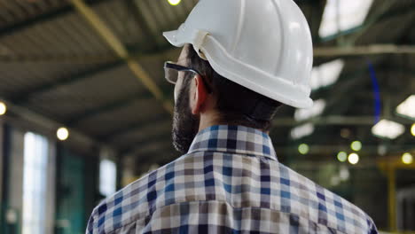 Rear-view-of-male-worker-in-a-plaid-shirt-and-a-helmet-walking-in-a-factory