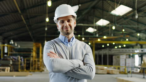 Caucasian-male-worker-wearing-a-helmet-and-posing-to-the-camera-with-crossed-arms-in-a-factory