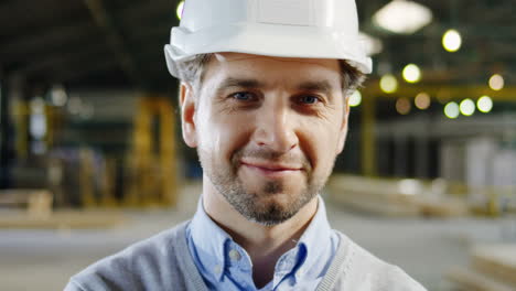 Close-up-view-of-caucasian-male-worker-wearing-a-helmet-and-posing-to-the-camera-in-a-factory