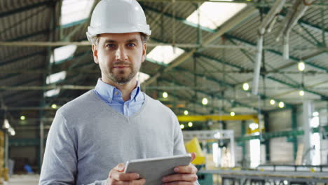 Caucasian-male-worker-wearing-a-helmet-using-a-tablet-and-looking-at-the-camera-in-a-factory