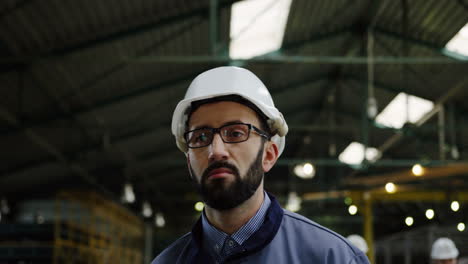 Close-up-view-of-the-male-factory-worker-wearing-a-helmet-and-glasses-walking-in-a-big-factory