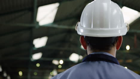 Rear-view-of-the-male-factory-worker-wearing-a-helmet-and-glasses-walking-in-a-big-factory