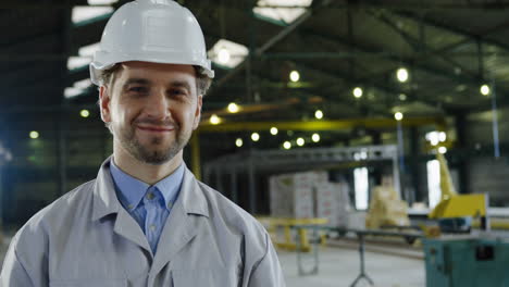 Close-up-view-of-Caucasian-engineer-wearing-a-helmet-and-looking-at-the-camera-in-a-big-factory