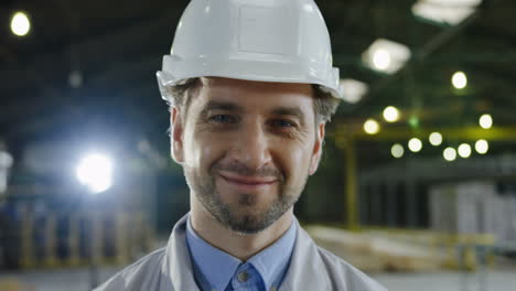 Close-up-view-of-Caucasian-engineer-wearing-a-helmet-and-turning-his-head-to-the-camera-and-smiling-in-a-factory