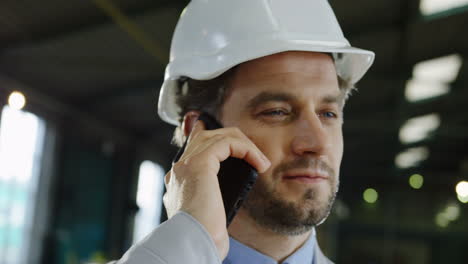 Close-up-view-of-engineer-wearing-a-helmet-and-talking-on-the-phone-in-a-factory