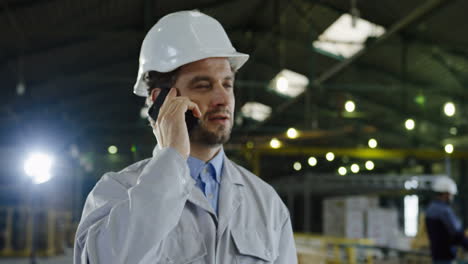 Caucasian-engineer-wearing-a-helmet-and-talking-on-the-phone-in-a-factory