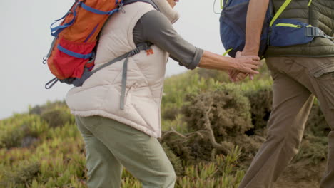 Senior-man-and-woman-holding-hands-and-climbing-the-mountain