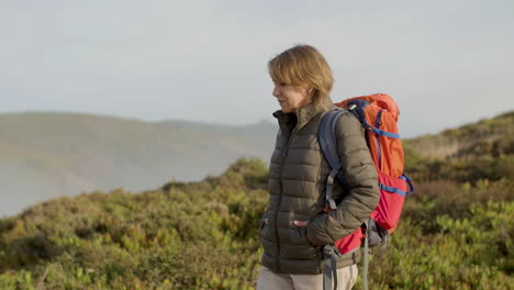Tracking-shot-of-a-senior-woman-with-backpack-walking-on-mountains-and-looking-around