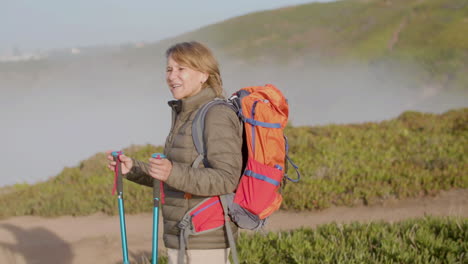 Tired-woman-with-backpack-hiking-on-mountains-with-trekking-poles,-then-having-break-and-leaning-on-sticks