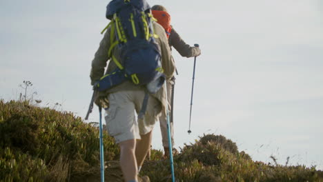 Caucasian-senior-couple-climbing-mountain-with-trekking-poles-and-admiring-the-landscape