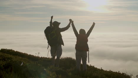 Back-view-of-happy-senior-hikers-raising-hands-while-standing-on-the-top-of-a-mountain