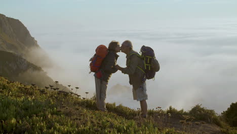 Senior-couple-standing-on-mountain,-holding-hands-and-kissing