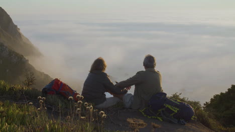 Senior-couple-sitting-on-top-of-mountain-and-kissing