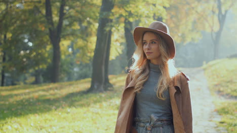 Caucasian-woman-with-blonde-hair-wearing-a-coat-and-hat-walking-in-the-park-in-the-morning-in-autumn