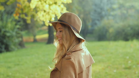 Caucasian-young-blonde-woman-walking-in-the-park-in-autumn-and-turning-to-the-camera-with-a-nice-small