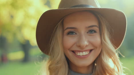 Close-up-view-of-Caucasian-young-blonde-woman-wearing-a-hat-smiling-and-hiding-her-face-behind-a-yellow-autumn-leaf-in-the-park