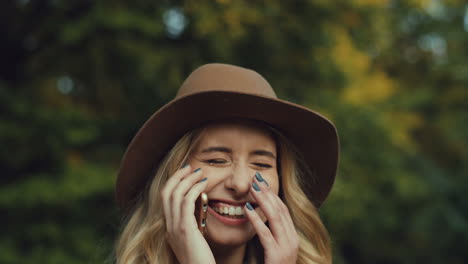 Close-up-view-of-caucasian-young-blonde-woman-wearing-a-hat-and-talking-on-the-phone-and-laughing-in-the-park-in-autumn