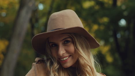 Close-up-view-of-caucasian-young-blonde-woman-in-a-hat-smiling-and-looking-at-camera-in-the-park-in-autumn