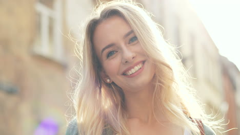 Close-up-view-of-blonde-young-woman-smiling-at-the-camera-while-standing-in-the-street