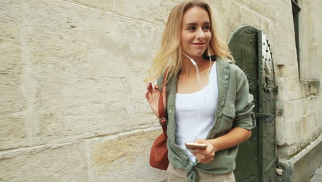 Close-up-view-of-caucasian-blonde-young-woman-walking-down-the-street-while-jumping-and-listening-to-music