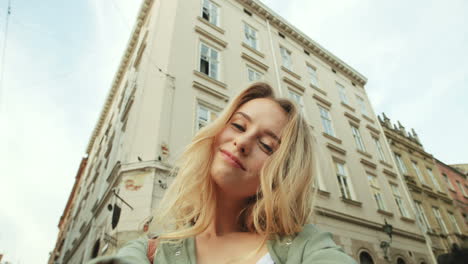 Close-up-view-of-caucasian-blonde-young-woman-smiling-and-posing-to-the-camera-in-the-street-while-holding-it