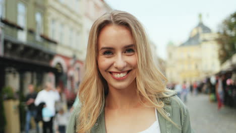 Close-up-view-of-Caucasian-blonde-woman-looking-straight-to-the-camera-while-taking-a-photo-in-the-street