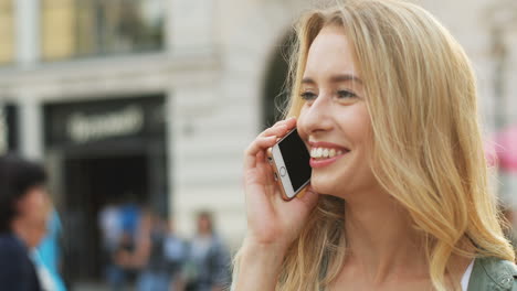 Close-up-view-of-Caucasian-blonde-woman-talking-on-the-smartphone-and-laughing-in-the-street
