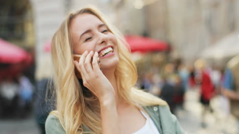 Close-up-view-of-Caucasian-blonde-woman-talking-on-the-smartphone-and-laughing-in-the-street