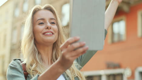 Close-up-view-of-blonde-young-woman-making-a-video-call-on-the-tablet-and-walking-down-the-street
