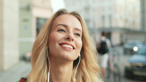 Close-up-view-of-Caucasian-blonde-woman-walking-down-the-street-and-listening-to-music-with-headphones
