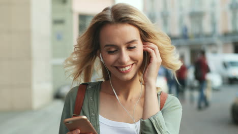 Close-up-view-of-Caucasian-blonde-woman-walking-down-the-street-and-listening-to-music-with-headphones