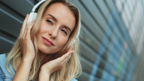 Close-up-view-of-blonde-young-woman-listening-to-music-with-headphones-and-singing-in-the-street
