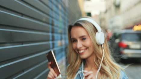 Caucasian-blonde-young-woman-listening-to-music-with-headphones-and-dancing-in-the-street