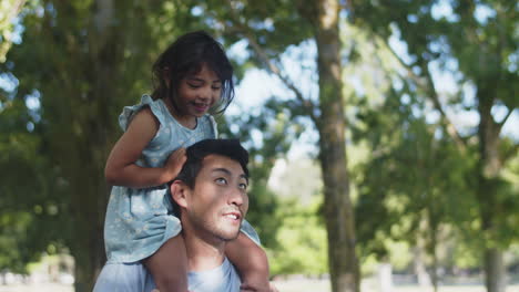 Happy-Asian-girl-riding-her-father-piggyback-in-park