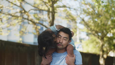 Happy-Asian-daughter-riding-father-piggyback-and-kissing-him