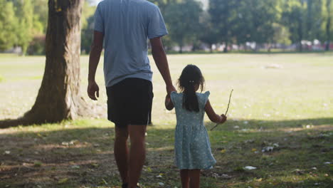 Rear-view-of-man-walking-with-toddler-daughter-in-park
