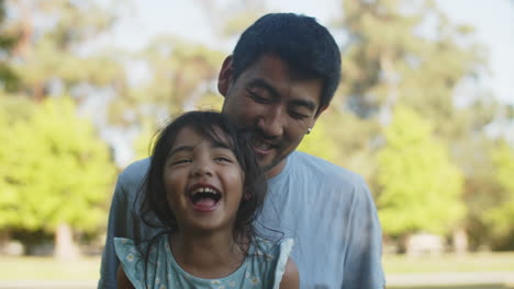 Portrait-of-happy-Asian-father-tickling-little-daughter-outdoors