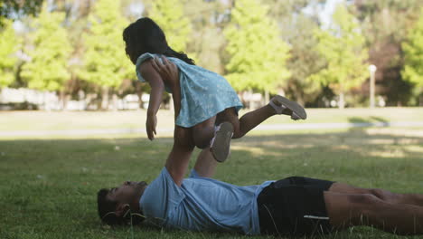 Happy-Asian-father-lying-on-grass-and-raising-little-daughter