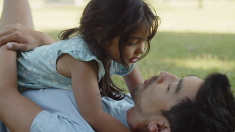 Little-girl-lying-with-father-on-ground-and-kissing-him-on-lips