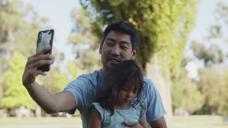 Feliz-Joven-Padre-Asiático-Tomando-Selfie-Con-Su-Hija-En-El-Parque-Al-Aire-Libre