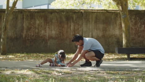Young-Asian-father-and-daughter-drawing-on-asphalt-with-chalks