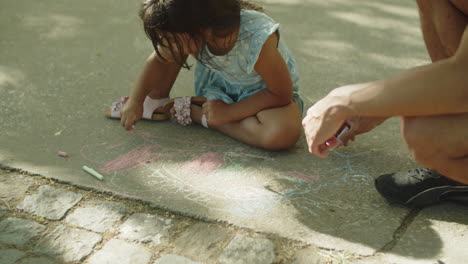 Father-and-child-sitting-on-asphalt-and-drawing-with-chalks