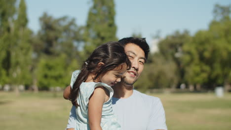 Feliz-Joven-Padre-Asiático-Caminando-Con-Una-Pequeña-Hija-En-Brazos-En-El-Parque