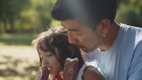 Close-up-of-happy-father-and-daughter-eating-chocolate-ice-creams-in-park