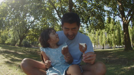 Portrait-of-happy-Asian-father-and-his-daughter-eating-chocolate-ice-creams-at-the-park
